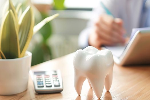 Patient working at a desk with prop tooth and calculator