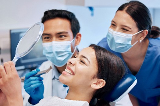 Dentist, dental assistant, and patient smiling at reflection in mirror