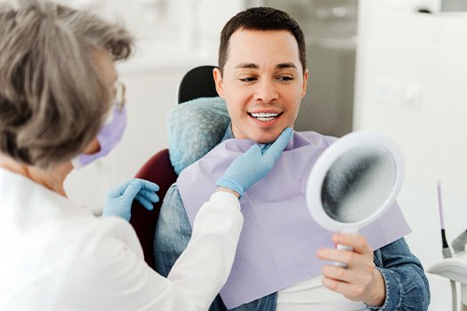 Man smiling at reflection in mirror with dentist