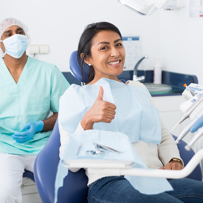 A smiling woman in a dentist’s chair giving a thumbs up