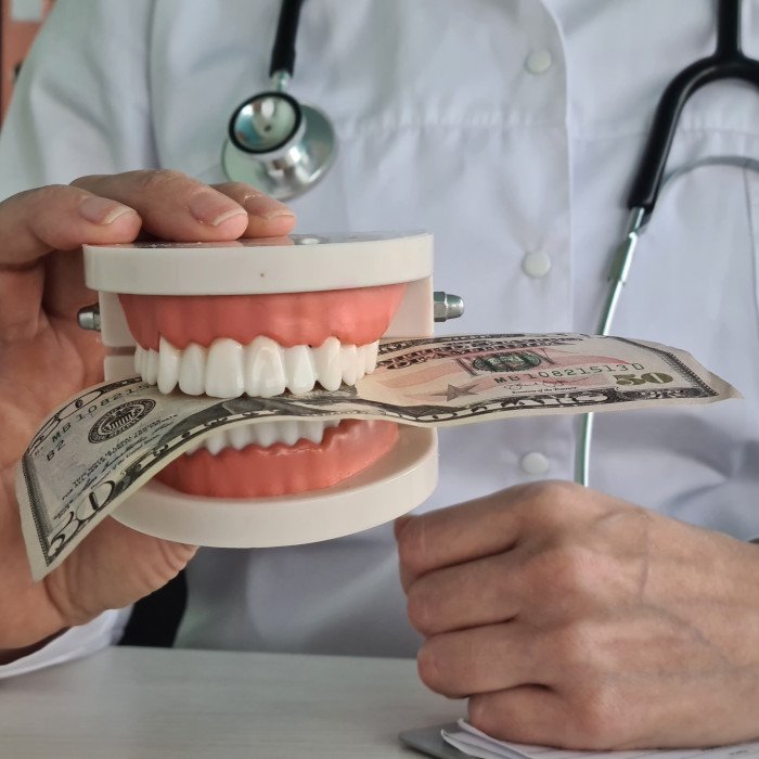 A dentist holding a model jaw clenching a 50-dollar bill