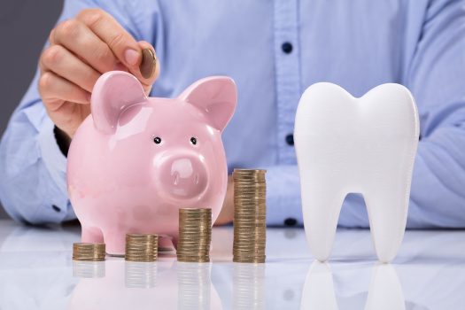 A man putting coins in a piggy bank next to a large model tooth