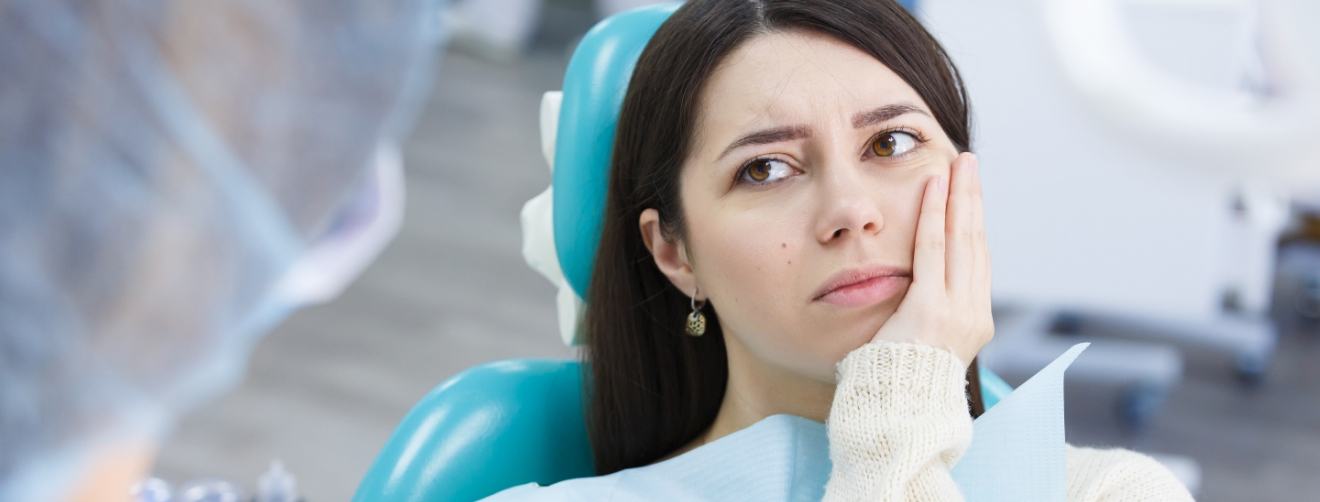 Woman wincing and holding her jaw in pain while talking to emergency dentist in Athens