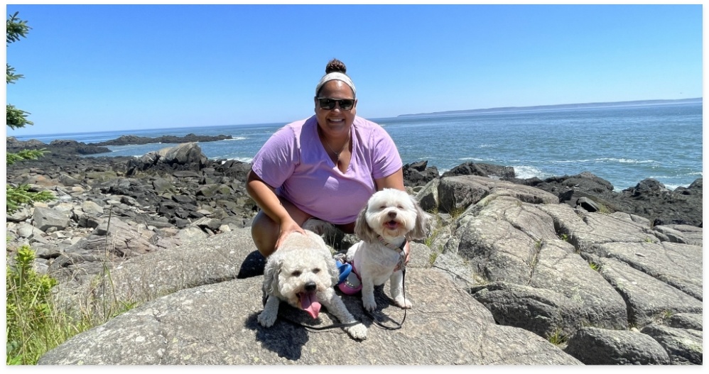 Doctor Moon smiling on rocky beach with two small fluffy white dogs