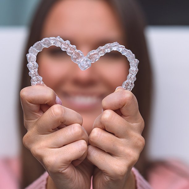 Woman holding clear aligners in the shape of a heart