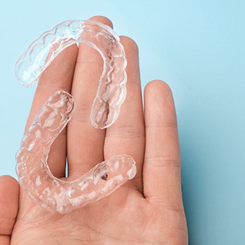 Two clear aligners resting on the palm of a hand with light blue background